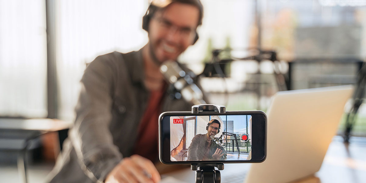 investing podcasts, young man presenting a podcast with his phone in the forefront of the image.