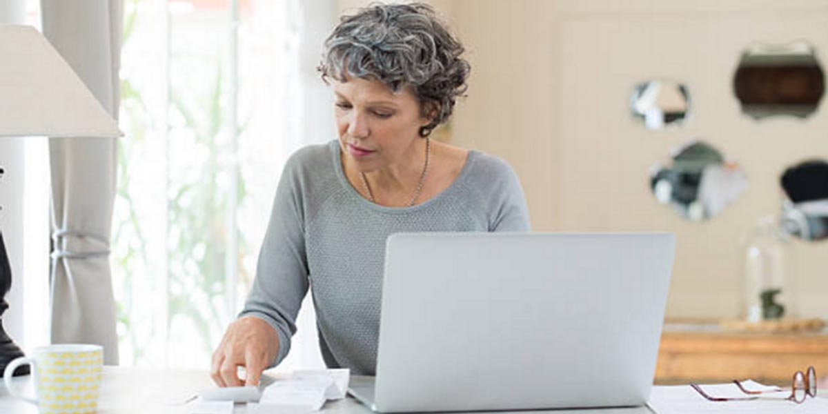 Planning to Work Past Your Retirement Age - lady with laptop looking at bills.